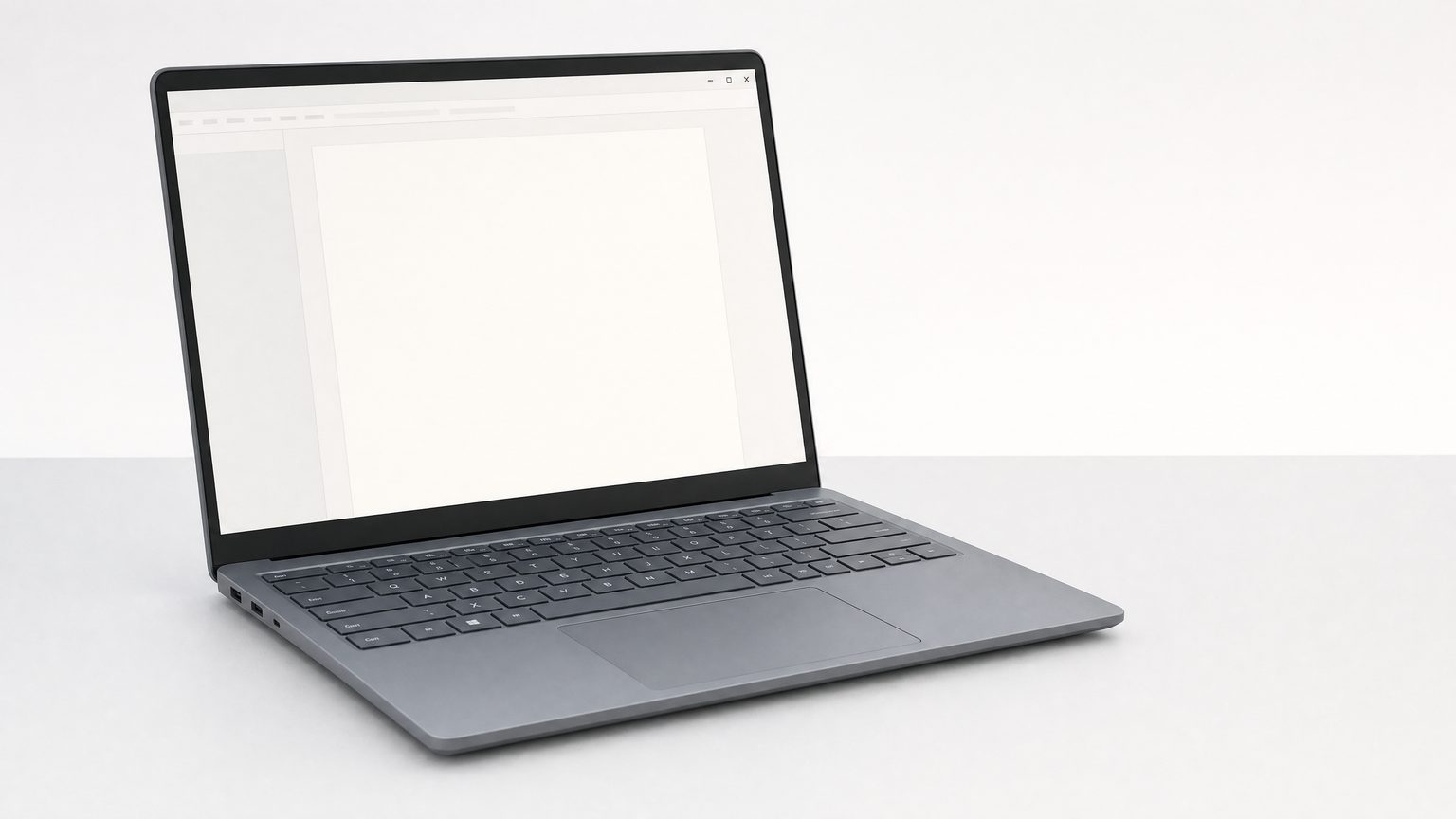 A thin Windows laptop on a plain grey desk, lid open, a blank document window on the screen.